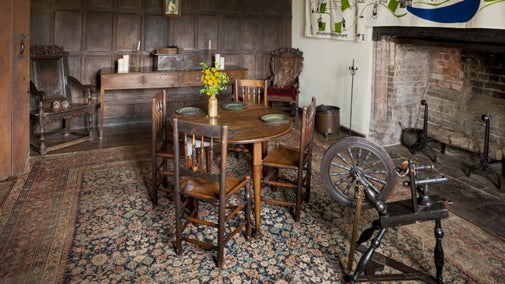 An interior view of the parlour at Brockhampton, with wood panelling on the far wall and a large open fireplace on the right, with wooden furniture including a table, chairs and spinning wheel